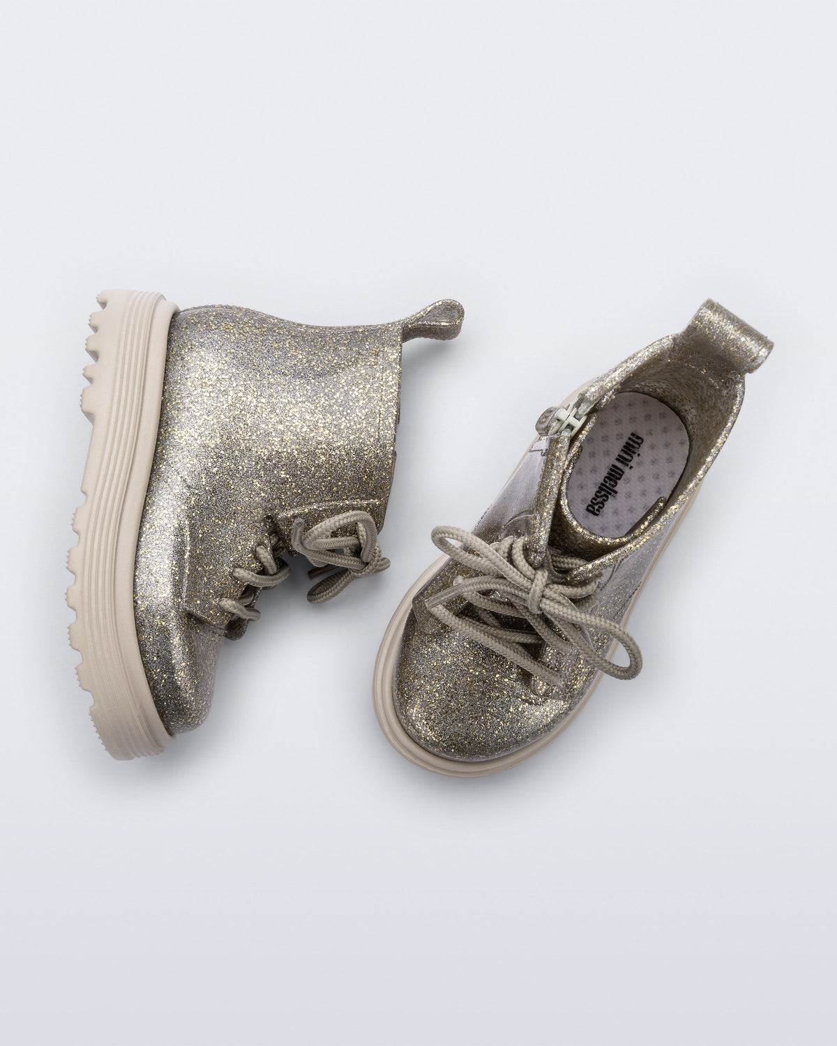 Side and top view of a pair of beige/golden glitter Coturno lace up baby boots
