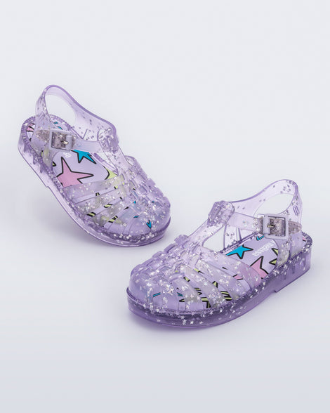 Angled view of a pair of clear lilac Possession baby sandals with star glitter