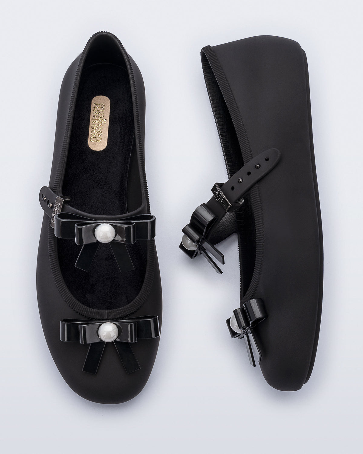 Top and side view of a pair of black Soft Ballerina Bow flats with bows and a pearl in the center of each bow