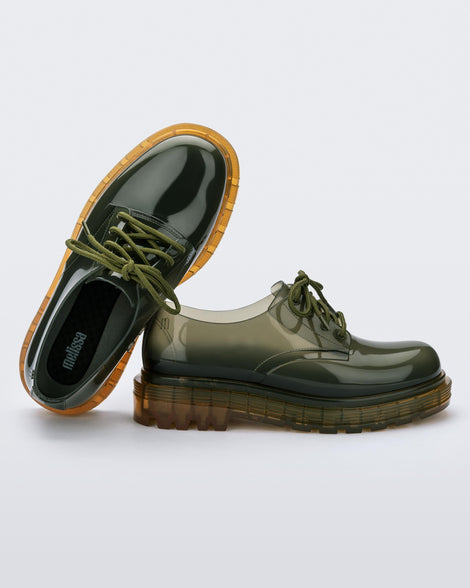 A front and side view of a pair of clear green / yellow Melissa Bass sneakers, with a transparent green base, green laces and a transparent yellow sole, leaning on eachother.