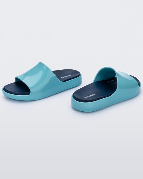 An angled side view of a pair of blue Mini Melissa Cloud slides with a navy blue insole and a lighter blue base.