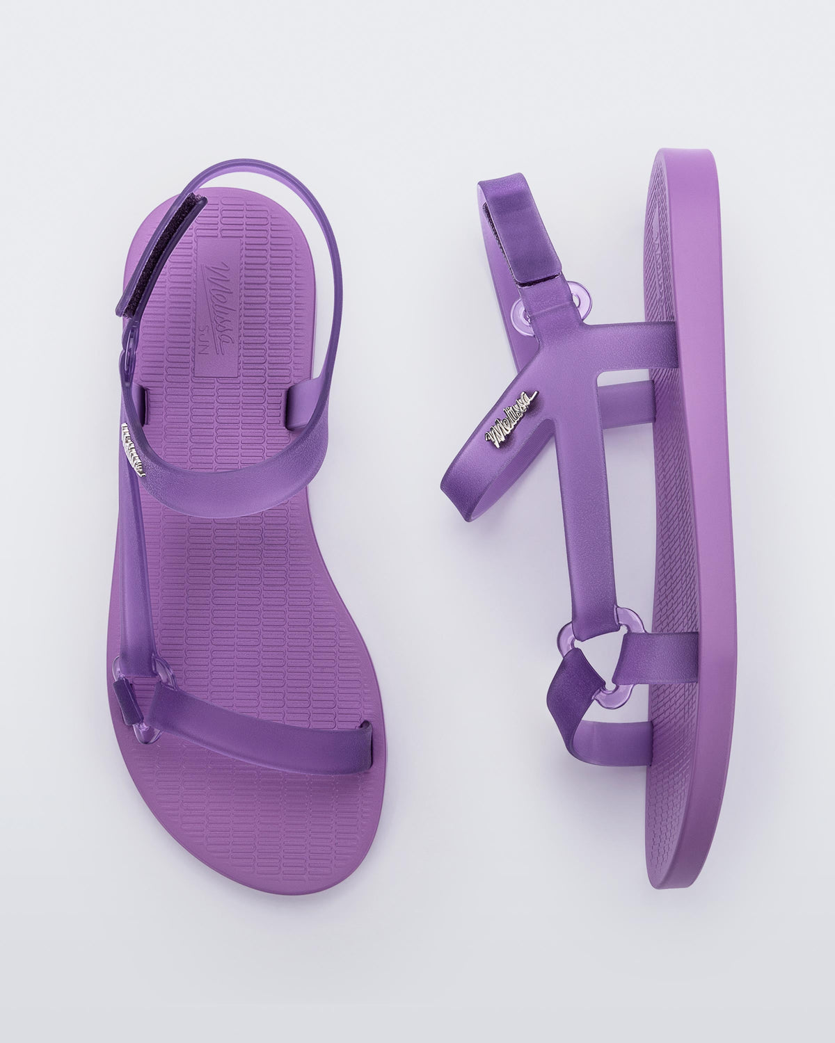Top and side view of a pair of Melissa Sun Downtown sandals with transparent lilac front cross and back ankle straps and a lilac purple sole.
