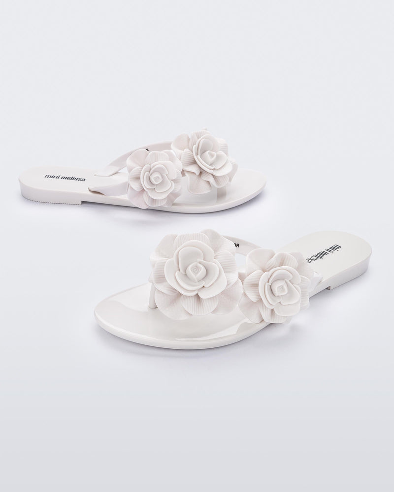 An angled front and side view of a pair of white Melissa Harmomic Squared Garden flip flops with flowers on the straps.