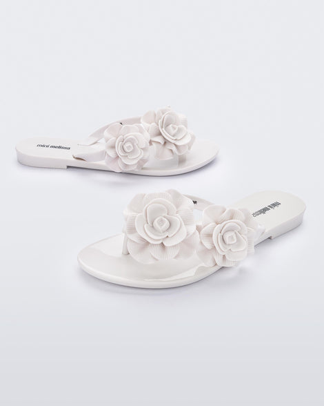 An angled front and side view of a pair of white Melissa Harmomic Squared Garden flip flops with flowers on the straps.