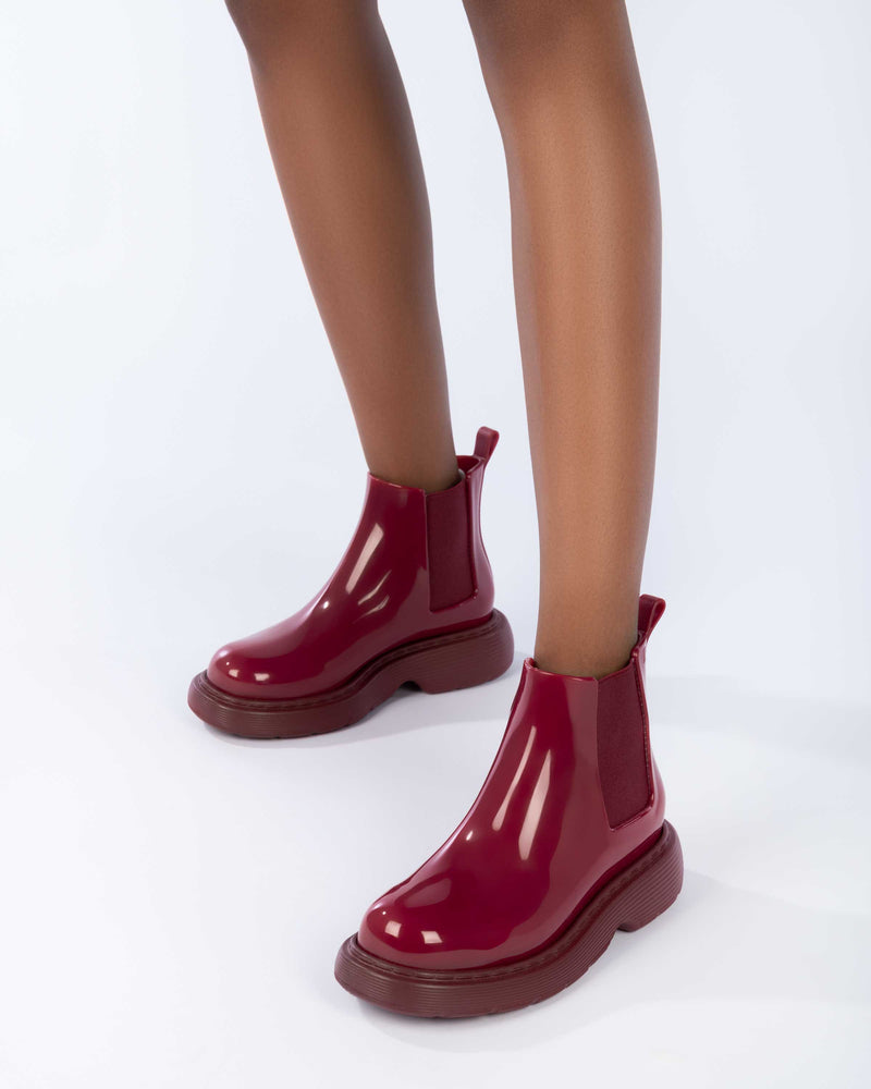 Close up of a model's legs wearing a pair of Melissa Step slip on ankle boots in Red with stretch side detail and lugg sole
