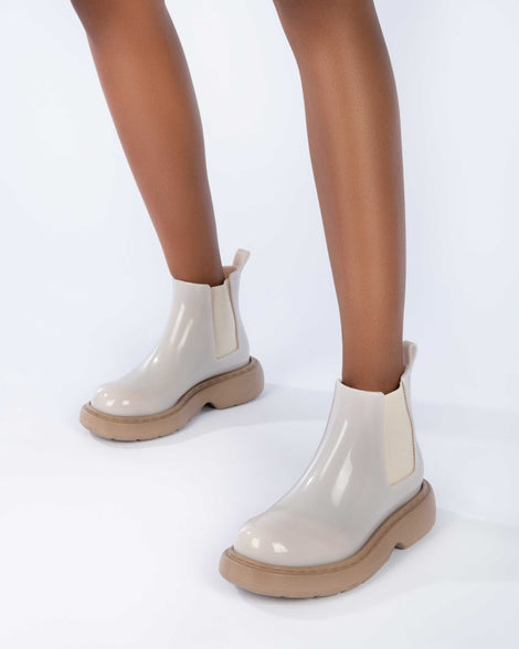 Closeup of a model's legs wearing a pair of Melissa Step slip on ankle boots with beige upper and brown lugg sole