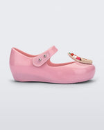 Side view of a Mini Melissa Ultra Girl Candy ballet flat in pink glitter colorway. The shoe has a single strap on the top of the foot with a double snap closure. The shoe has a 3D printed cupcake applicque with smiling face on the top of the toe. The colors of the applique are red, brown and white.