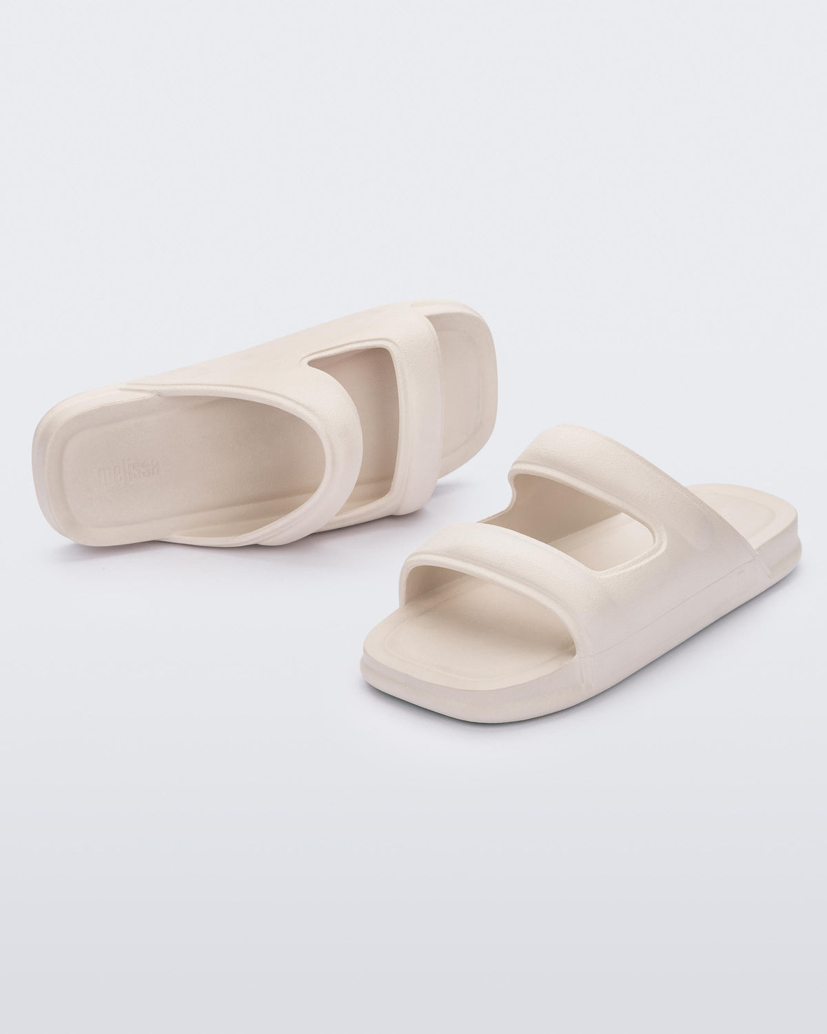 An angled front and side view of a pair of beige Melissa Free Grow slides with a square cut out on the front.