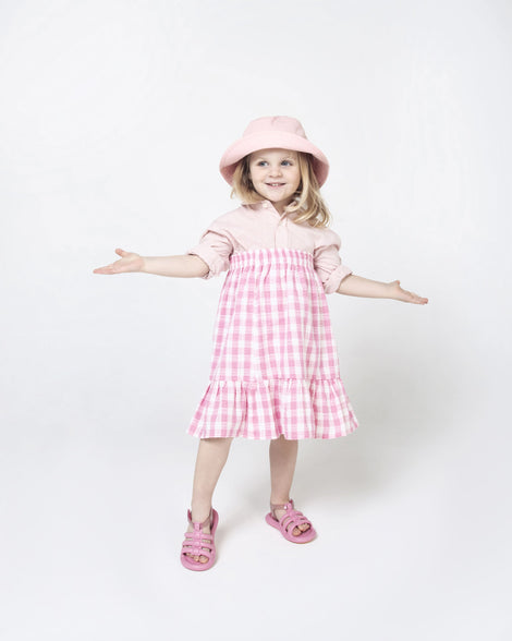 A model posing for a picture in a pink dress, hat and pink Mini Melissa Freesherman sandals with pink and clear glitter straps.