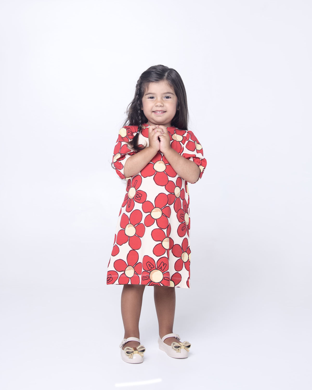 Little girl model in a red flower dress wearing a pair of beige Mini Melissa Sweet Love mary jane flats with metallic gold bow.