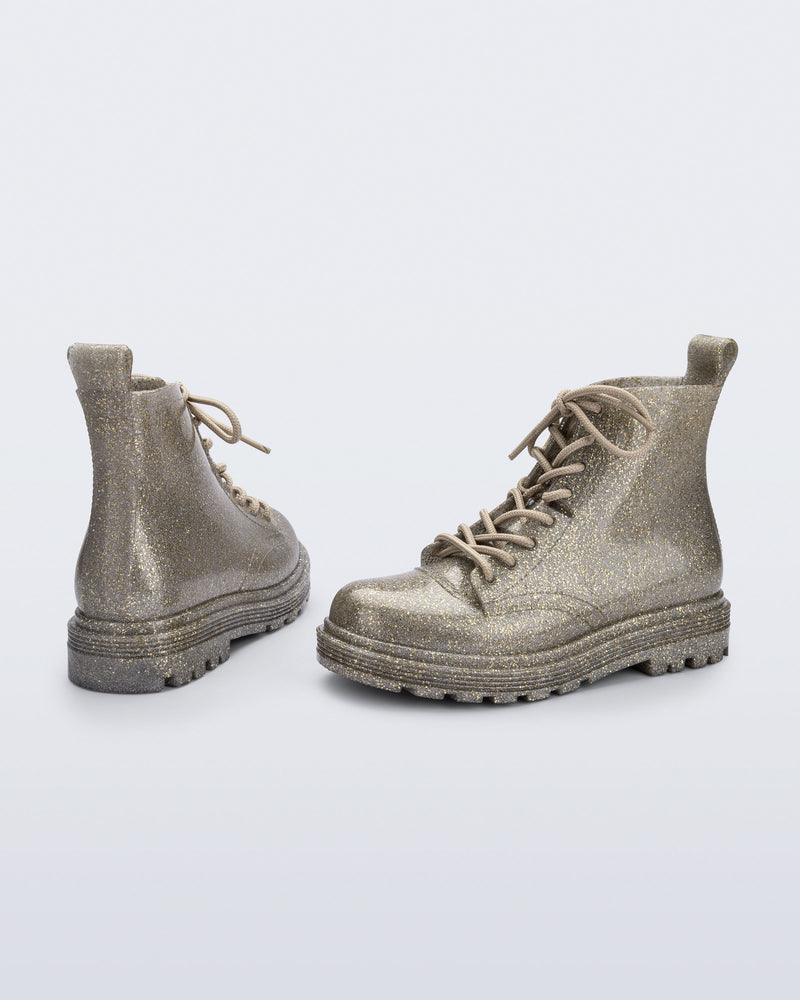 Angled view of a pair of Mini Melissa lace up Coturno boots in gold glitter color-way