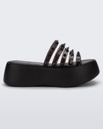 Side view of a Black/Clear Black Melissa Punk Love Becky platform slide with a black base and several top straps with spike stud details.