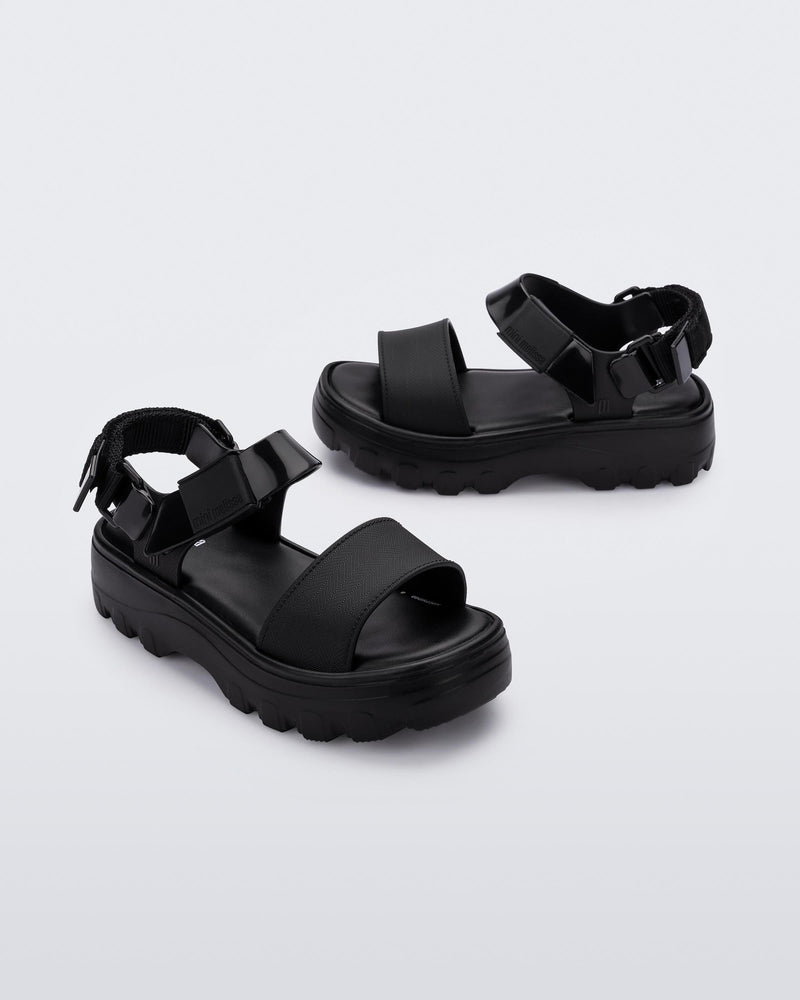 Angled view of a pair of Mini Melissa Kick Off platform sandals in black with adjustable velcro ankle straps