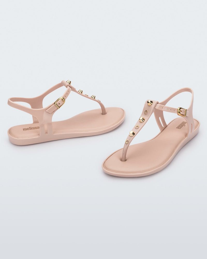 Angled and side view of a pair of pink Melissa Solar studs sandals with gold studded t-strap and gold buckle.