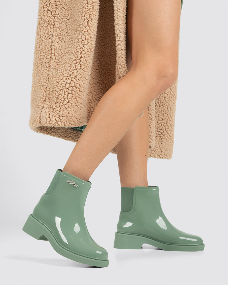 Model's legs wearing a pair of sage green Chelsea Boots.