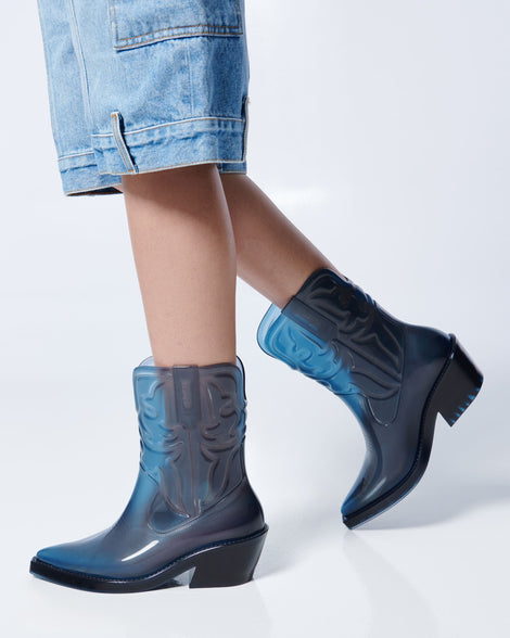 Models legs in long jean shorts wearing a pair of transparent blue Texas boots