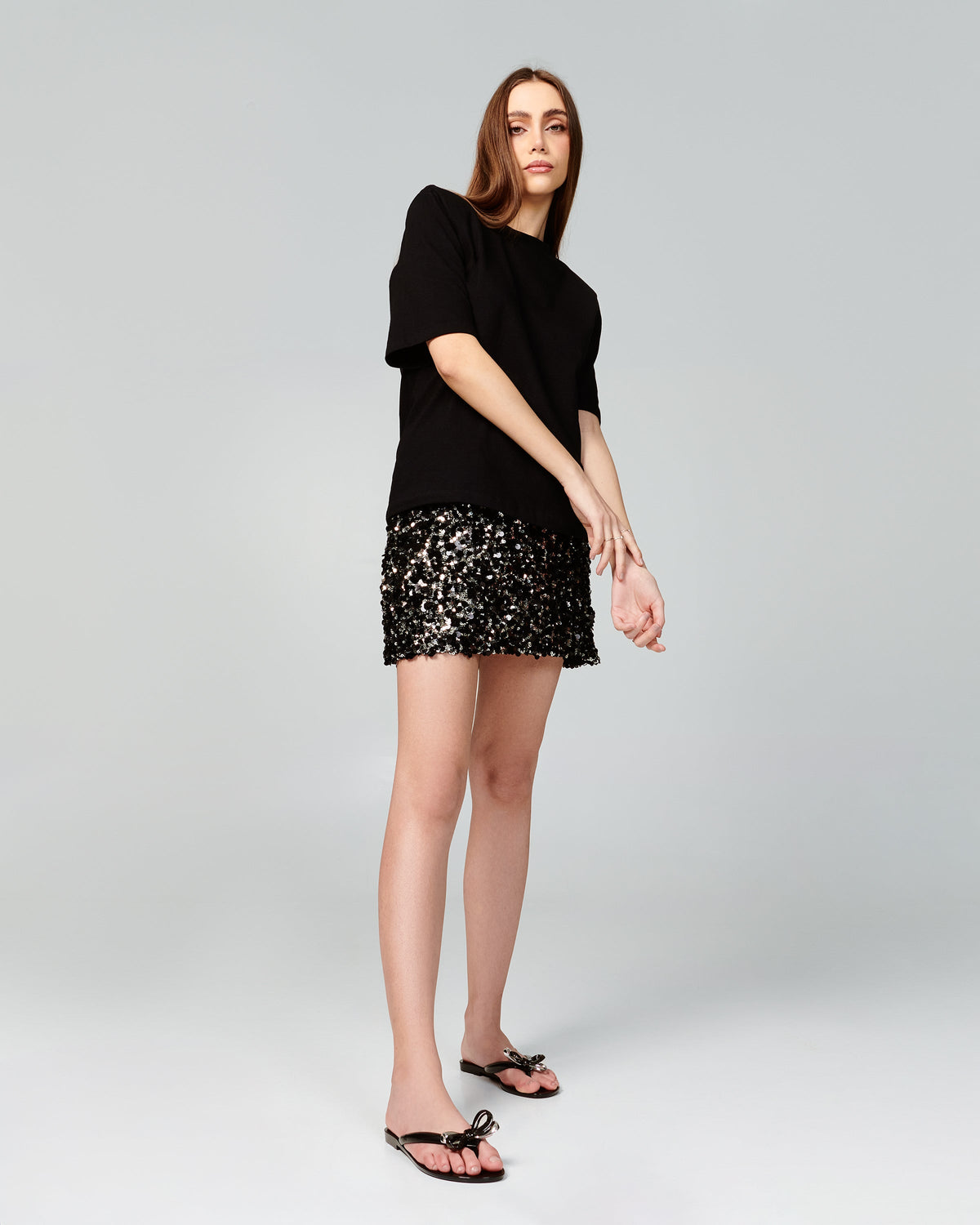 Model in a black sweater and sparkling skirt wearing a pair of black Harmonic Eclipse flip flops with bow.
