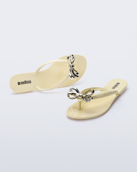 Top and angled view of a pair of beige Harmonic Eclipse flip flops with bow.