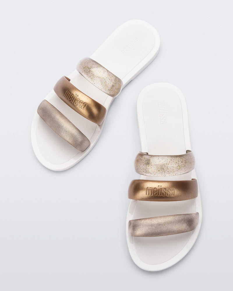 Top view of a pair of white Eclipse Slides with bronze straps.
