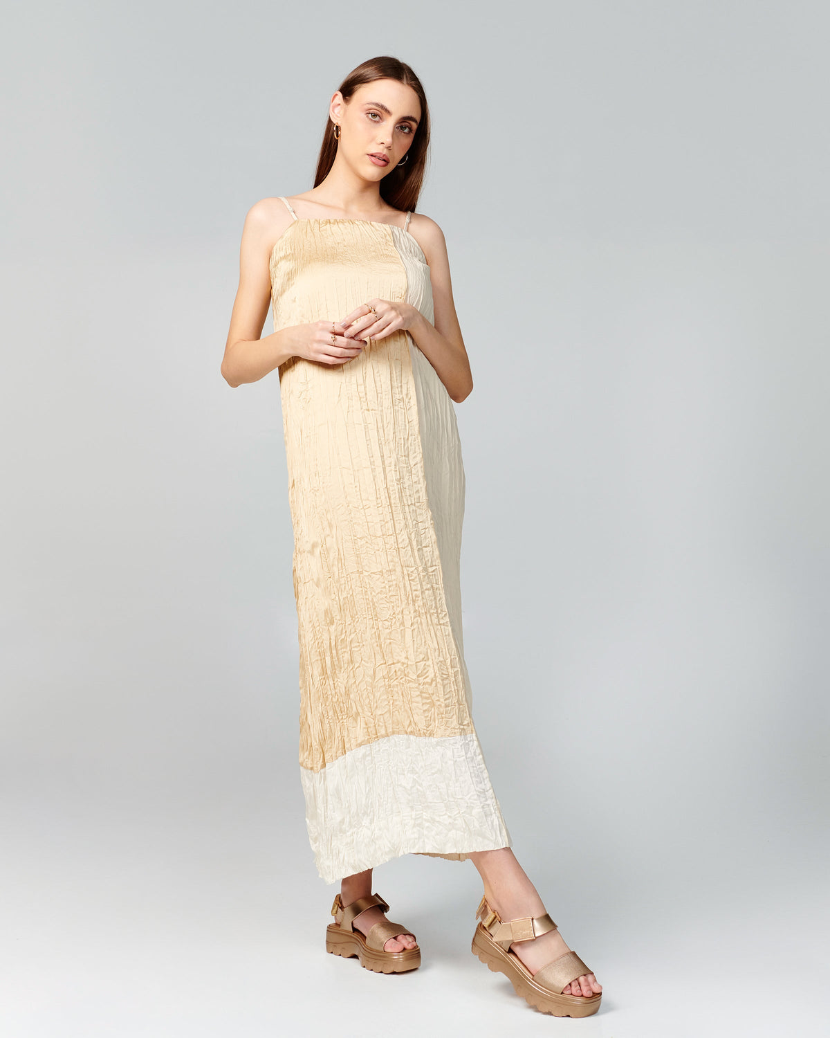 Model in a beige dress wearing a pair of gold Kick Off Sandals