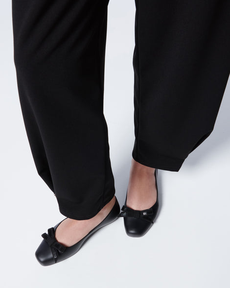 Close up of a model's legs wearing lack pants and Melissa Aura flats in black with a bow on a white background