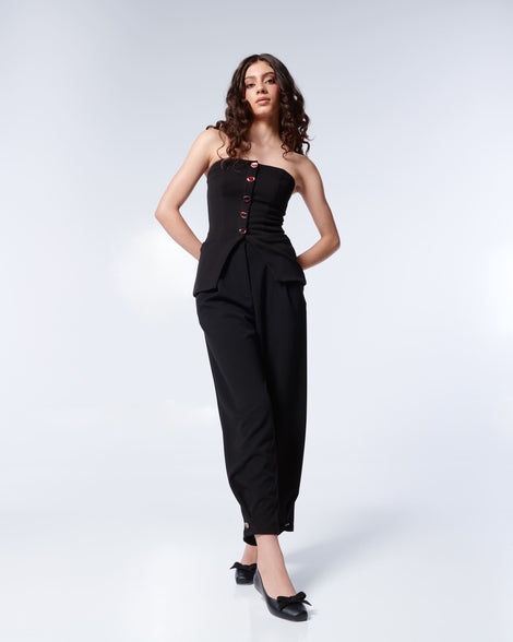 Woman posing wearing a black strapless jumpsuit with red buttons and the Melissa Aura flats in black.