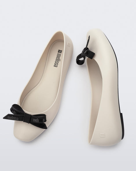 Pair of Melissa Aura flats in beige with black bows on a white background