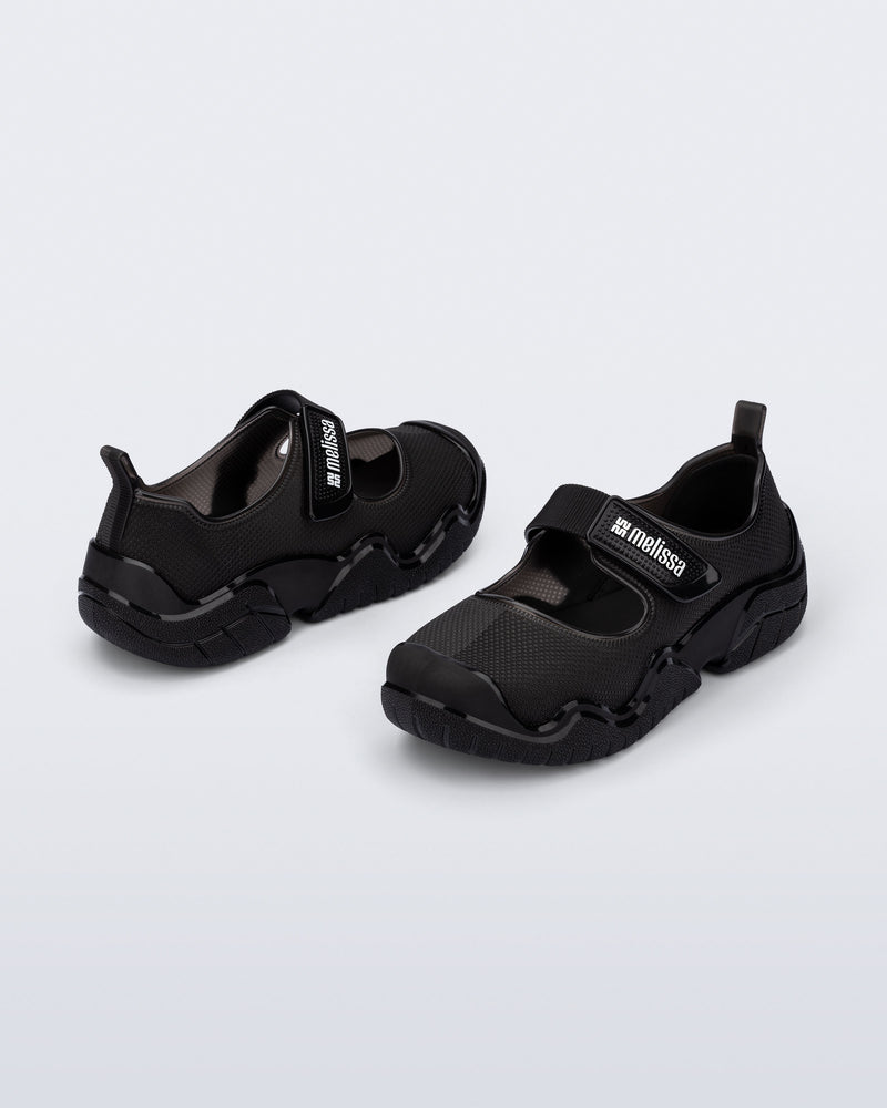 Angled view of a pair of the Melissa Sprint Ballerina flats in black with a velcro strap on a light gray background
