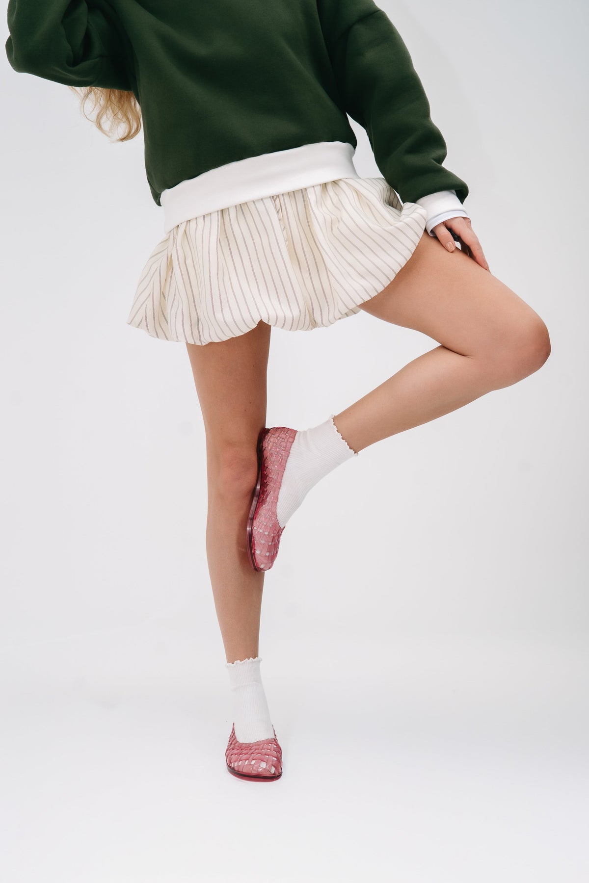 Model in a green sweater and beige skirt wearing a pair of clear pink Possession ballerinas with white socks