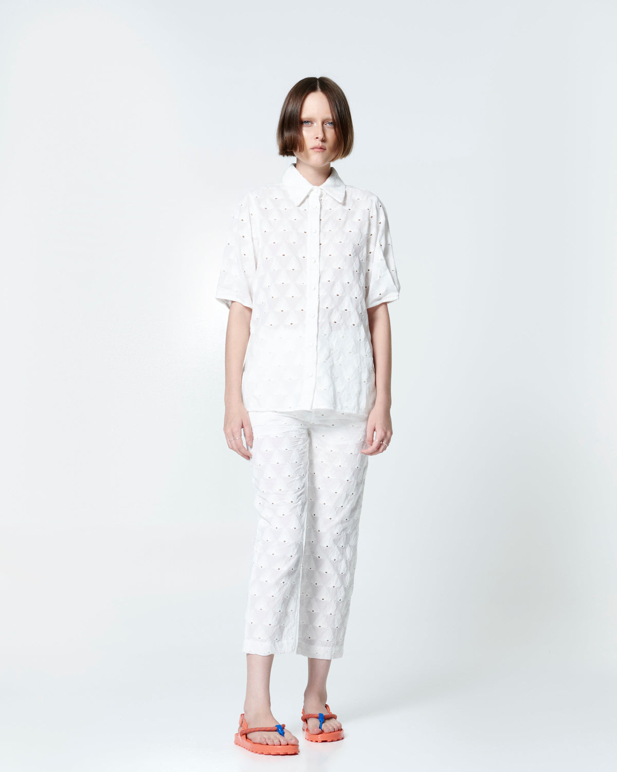 Model in a white pant set wearing a pair of orange Bond sandals with textile strap and blue toe piece