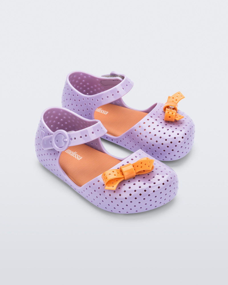 Angled view of a pair of lilac Pop baby flats with orange bow
