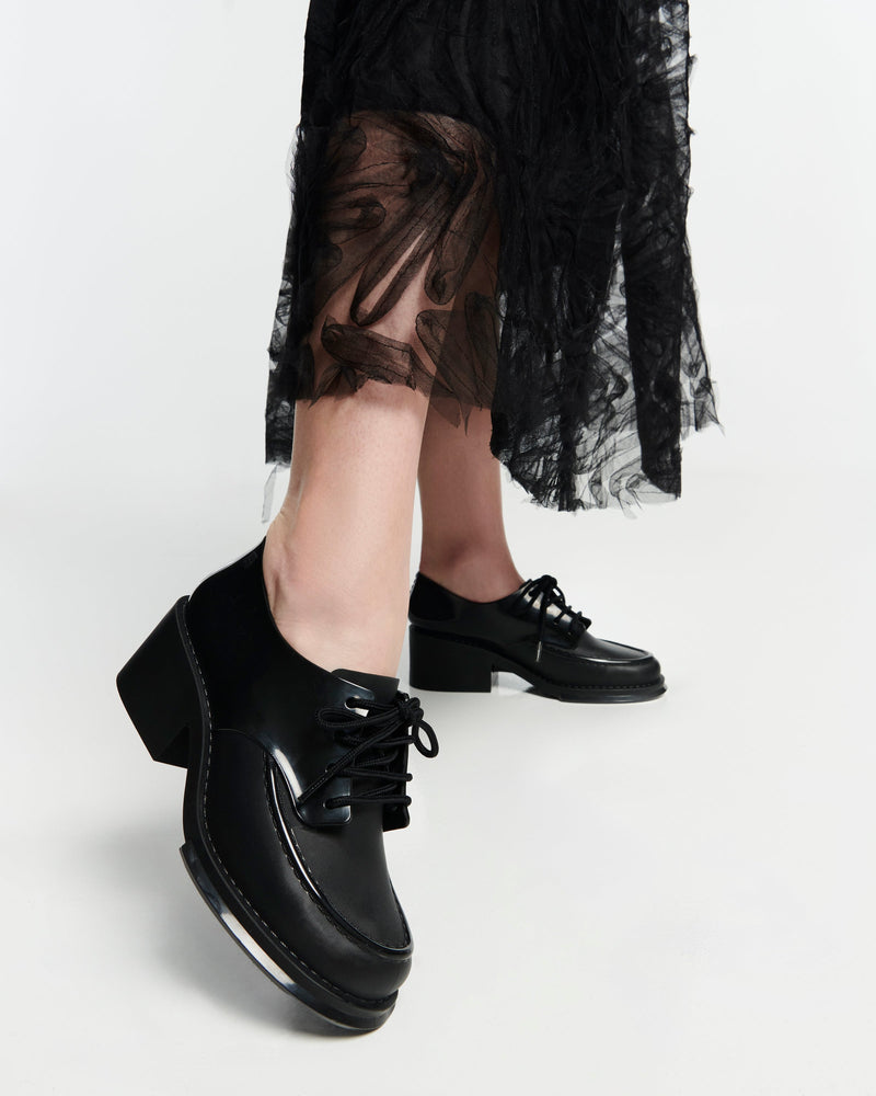 Model's legs in a black skirt wearing a pair of black Tailor loafers