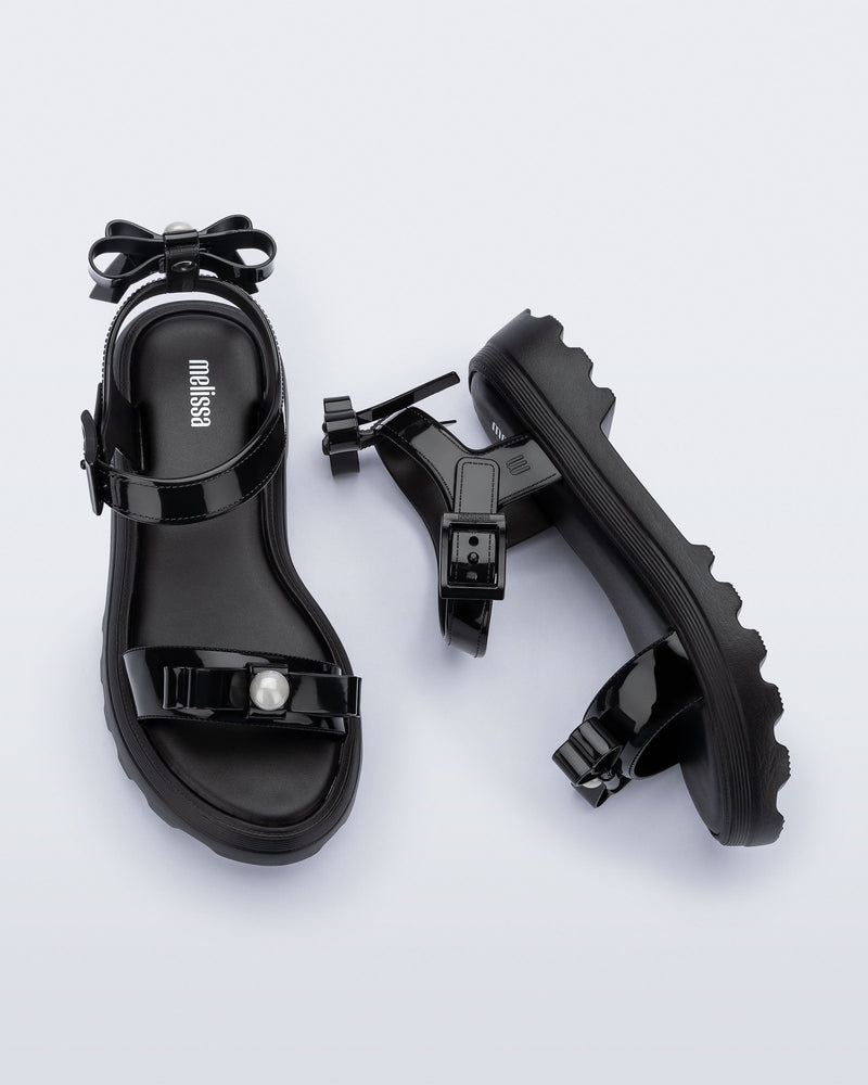 Side and top view of a pair of black Town Bow sandals with bows and a pearl in the center of each bow
