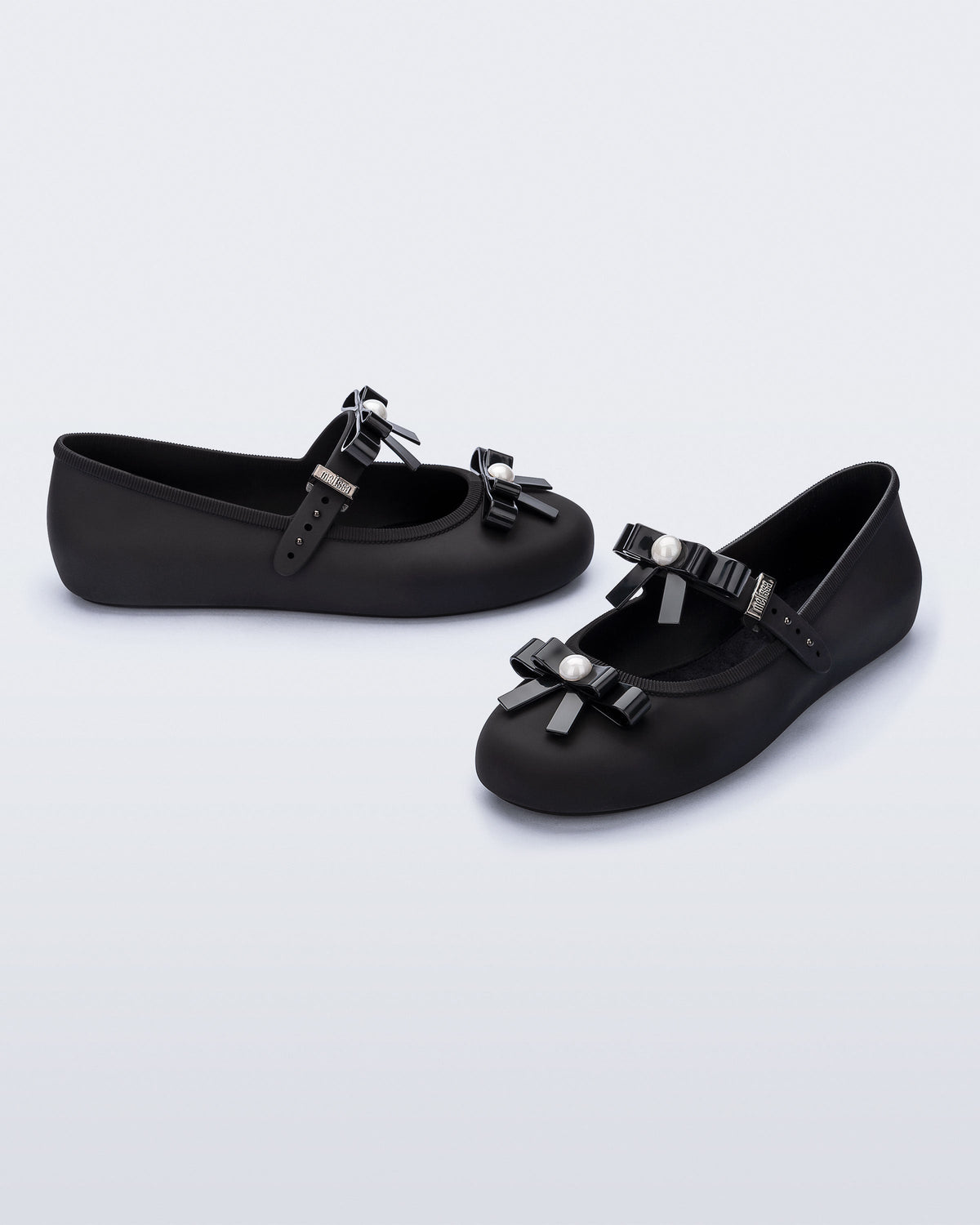Angled view of a pair of black Soft Ballerina Bow flats with bows and a pearl in the center of each bow