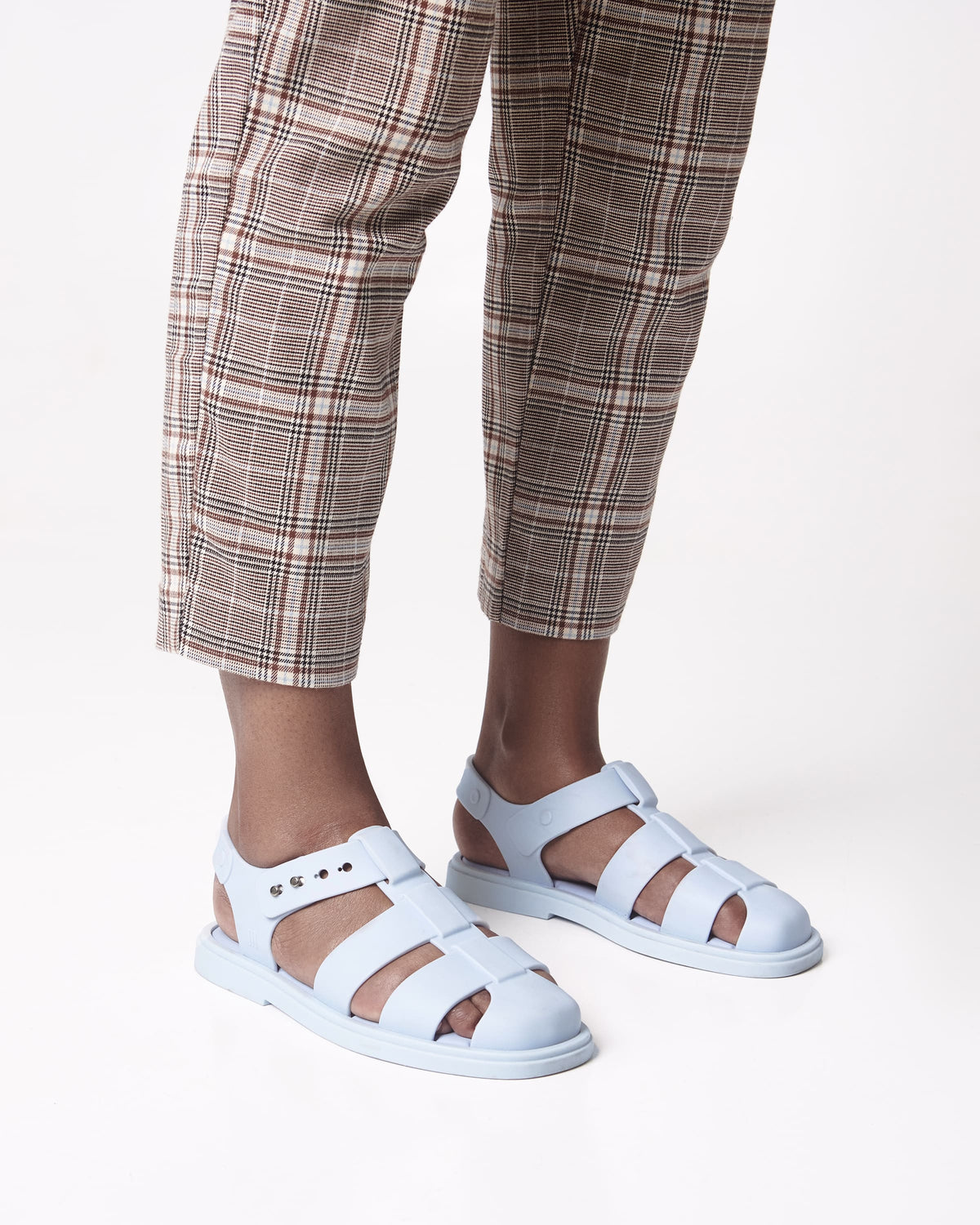 Model's legs in brown plaid pants wearing a pair of blue Emma women's sandals.