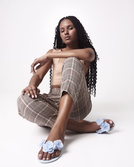Model in a tan shirt and brown patterned pants wearing a pair of blue Harmonic Springtime women's flip flop with 3 blue flowers.