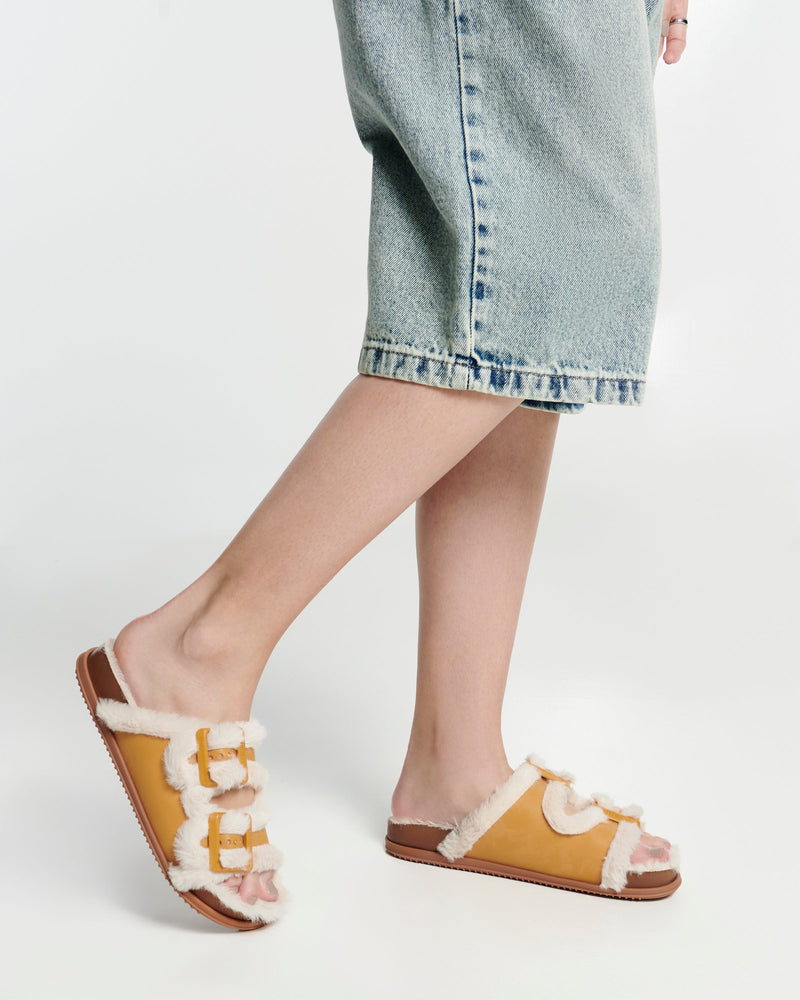Model's legs in long jean shorts wearing a pair of orange Cozy Warm Slides with beige fuzzy insoles
