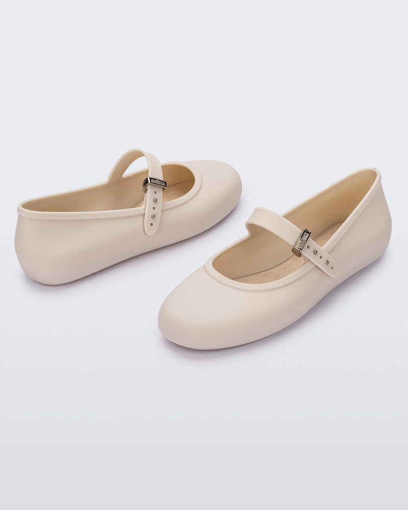 Angled view of a pair of beige Soft adult flats with strap and gold buckle