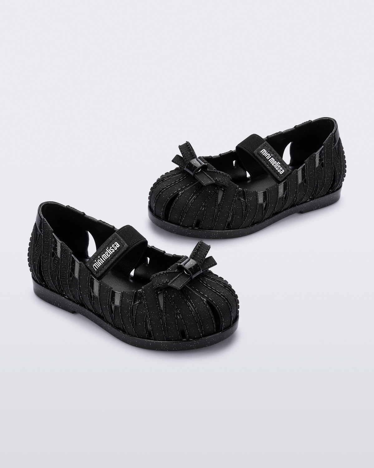Angled view of a pair of glitter black M Lover Ballerina baby flat with bow and strap
