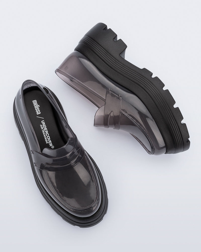 Top and side view of a pair of transparent smoke Royal High + Undercover platform loafers with black sole.