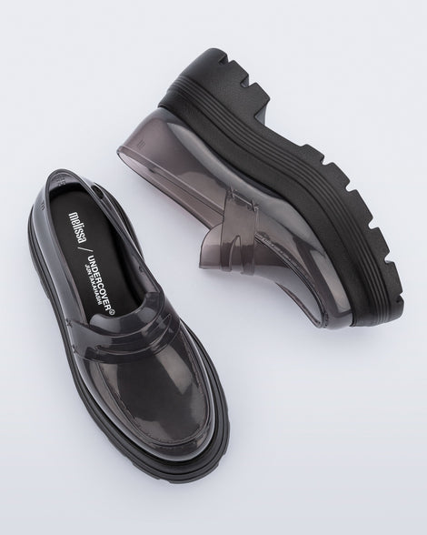 Top and side view of a pair of transparent smoke Royal High + Undercover platform loafers with black sole.