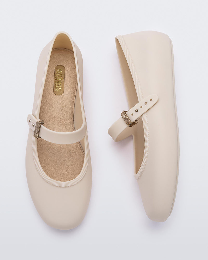 Top and side view of a pair of beige Soft adult flats with strap and gold buckle