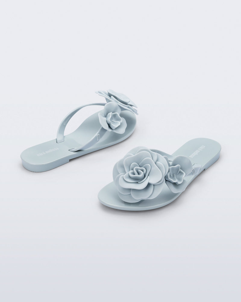 Back and angled view of a pair of blue Harmonic Petals kids flip flops with flowers