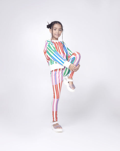 Model posing in a striped sweat suit wearing a pair of Mini Melissa Kick Off platform sandals in white with adjustable velcro ankle straps