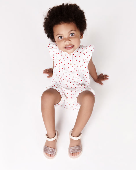 Toddler model in a white with red dots outfit wearing a pair of beige Mar Wave baby sandals.