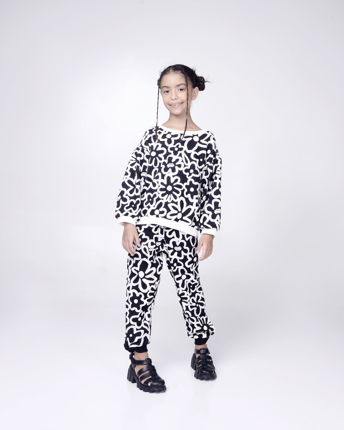 Child model in a black and white patterned outfit wearing a pair of black Megan kids heel sandals.