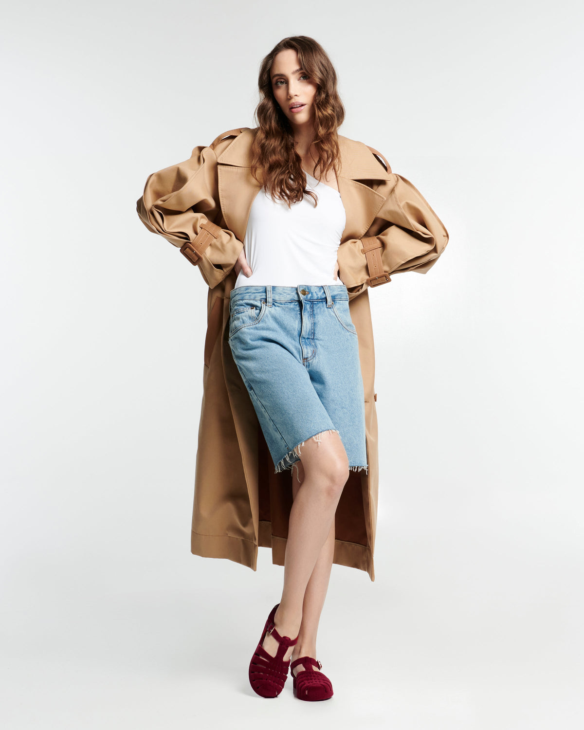 Model in jean shorts and white shirt and tan coat wearing a pair of flocked red Possession Velvet fisherman sandals