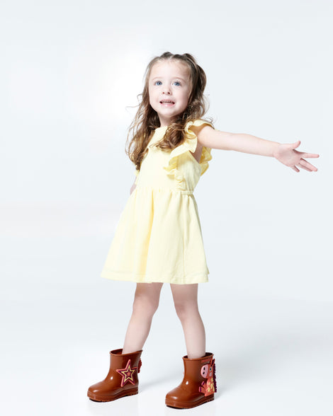 Child model in a yellow dress wearing a pair of brown Welly Wonderland baby boots with orange pony on one shoe and star on the other