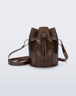 Side view of a Melissa Station bucket bag in Bronze. The bag has an adjustable shoulder strap and a drawstring top closure. The Melissa logo is on the bottom center of the front of the bag.