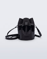 Side view of a Melissa Station bucket bag in Black. The bag has an adjustable shoulder strap and a drawstring top closure. The Melissa logo is on the bottom center of the front of the bag.
